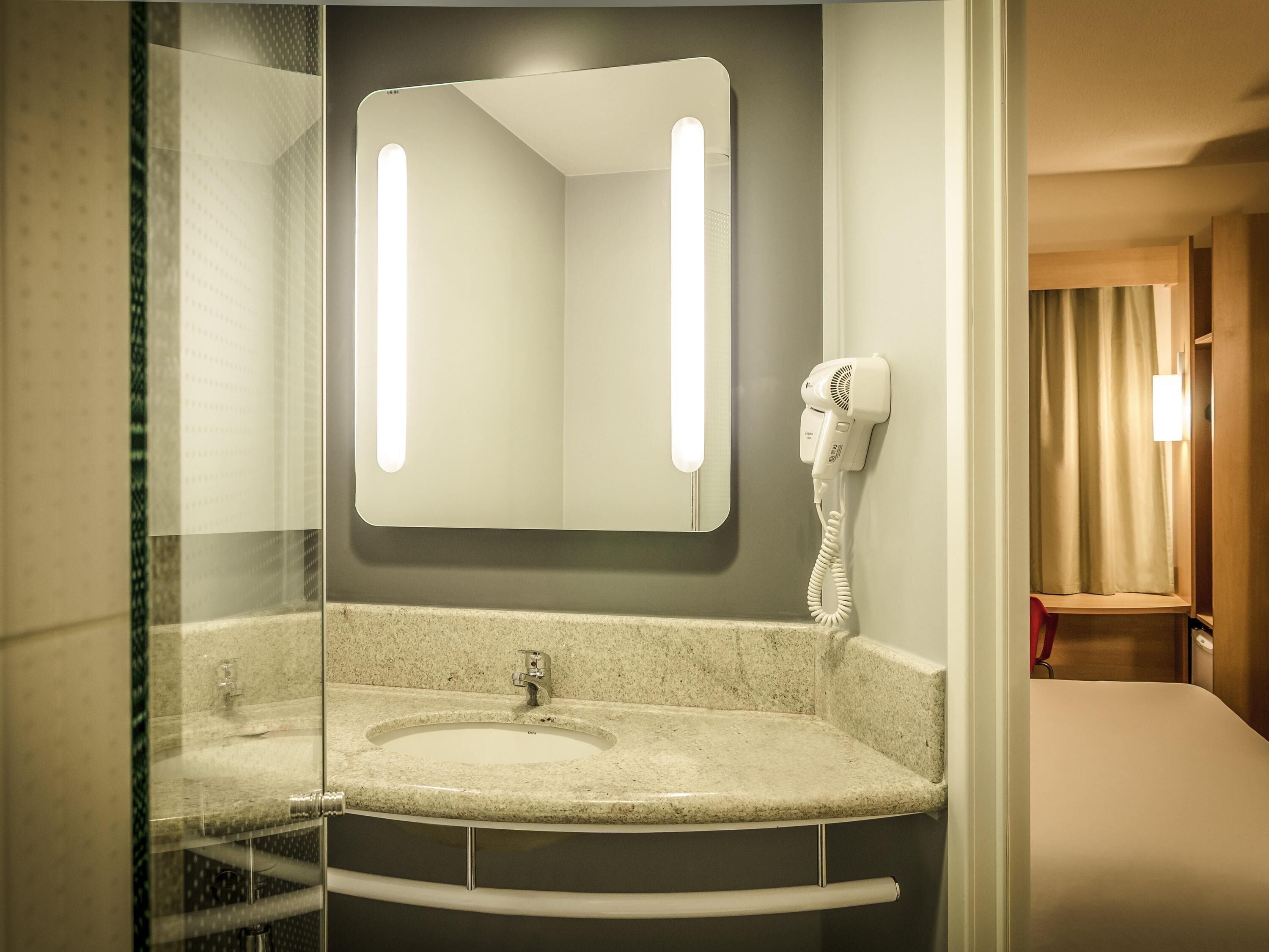 A bathroom with a sink, mirror, hairdryer, and a shower area.