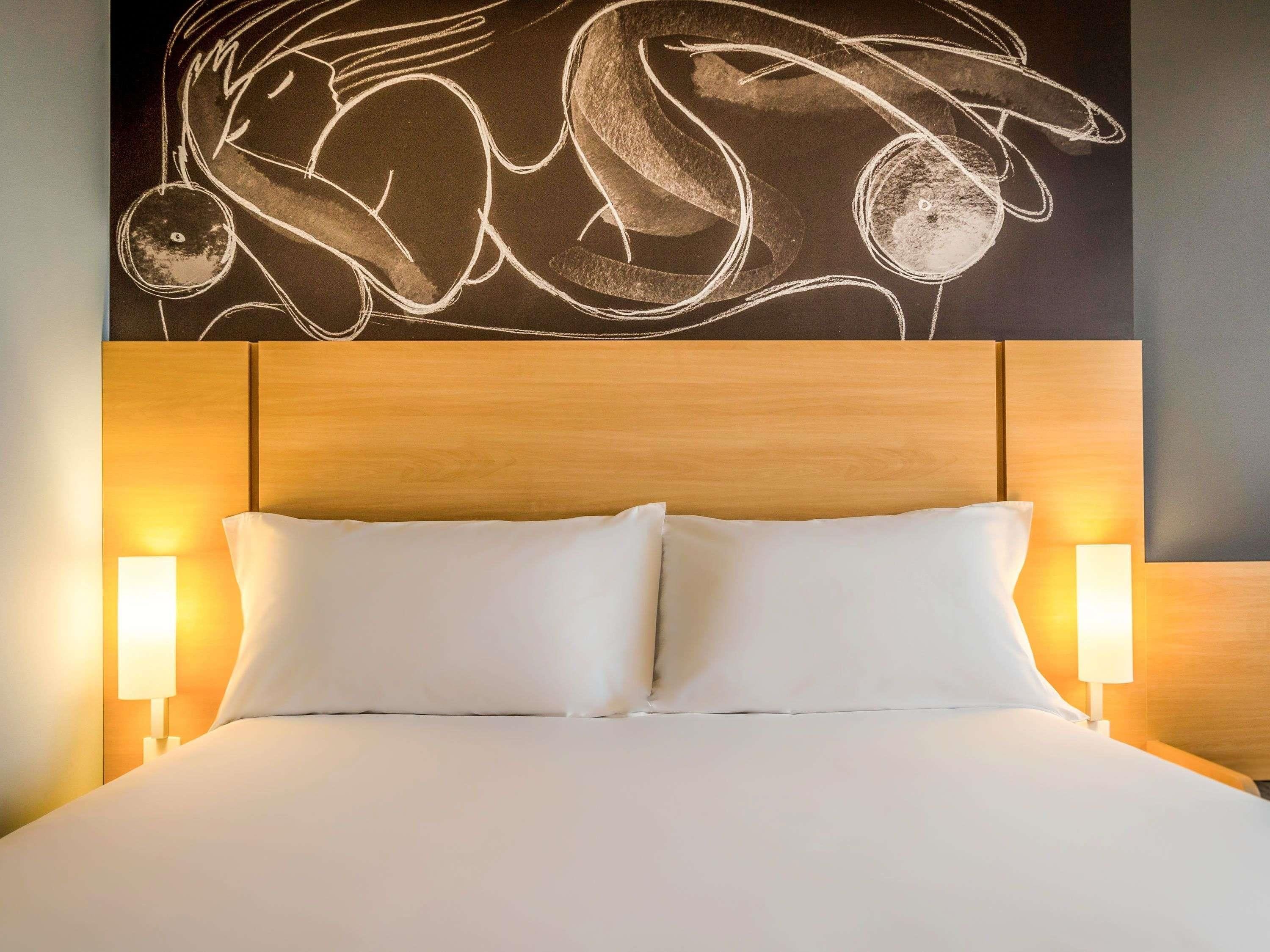 Una habitación de hotel con una cama grande, dos lámparas de noche y una pared decorada con arte abstracto.