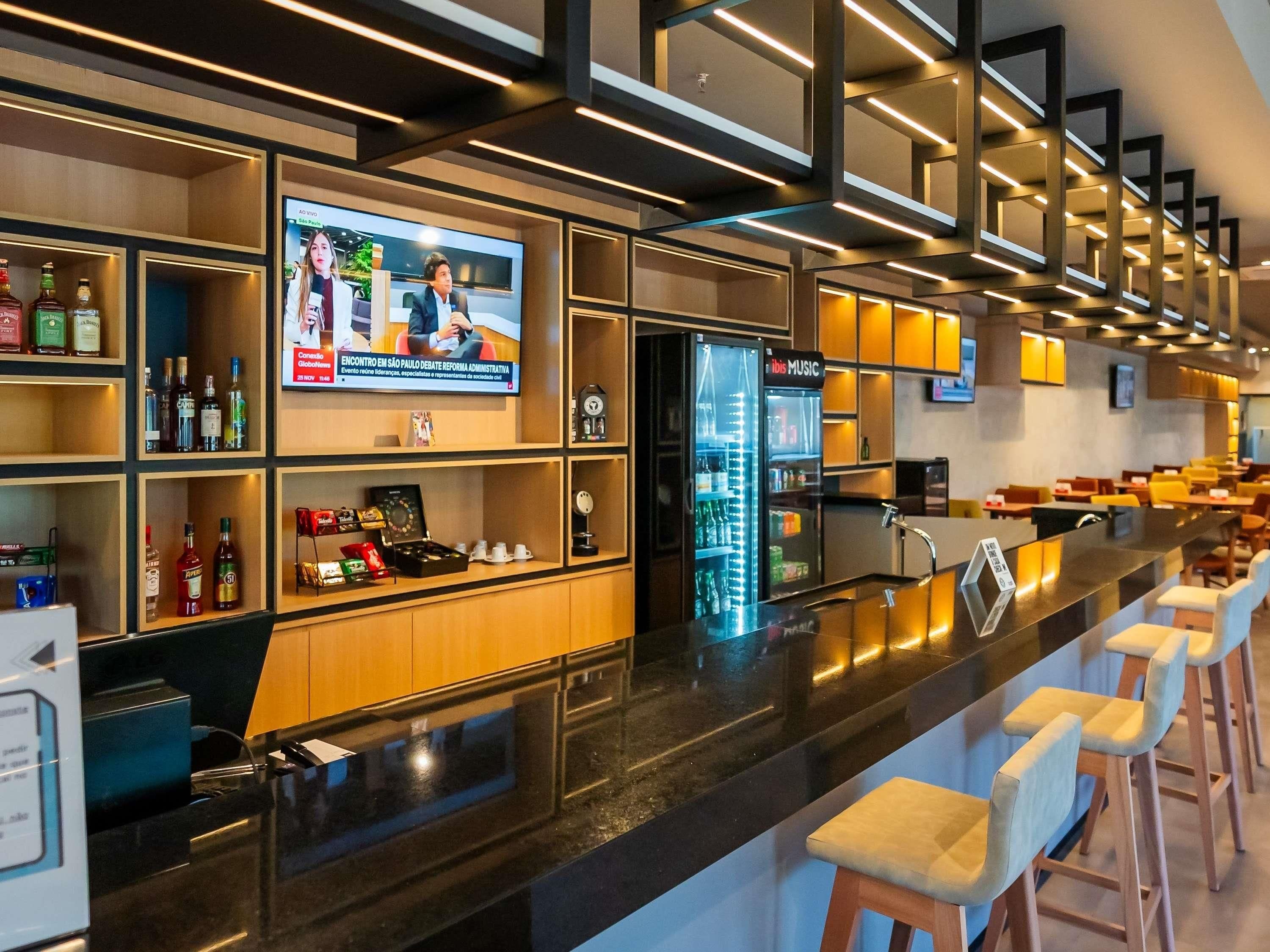 Zona de bar moderna con televisor de pantalla plana, estantes con botellas, un minibar y taburetes.