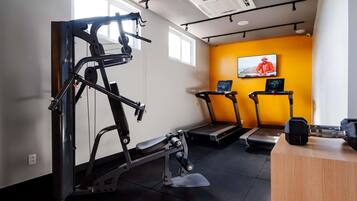 A gym with exercise equipment, treadmills, and a wooden desk.