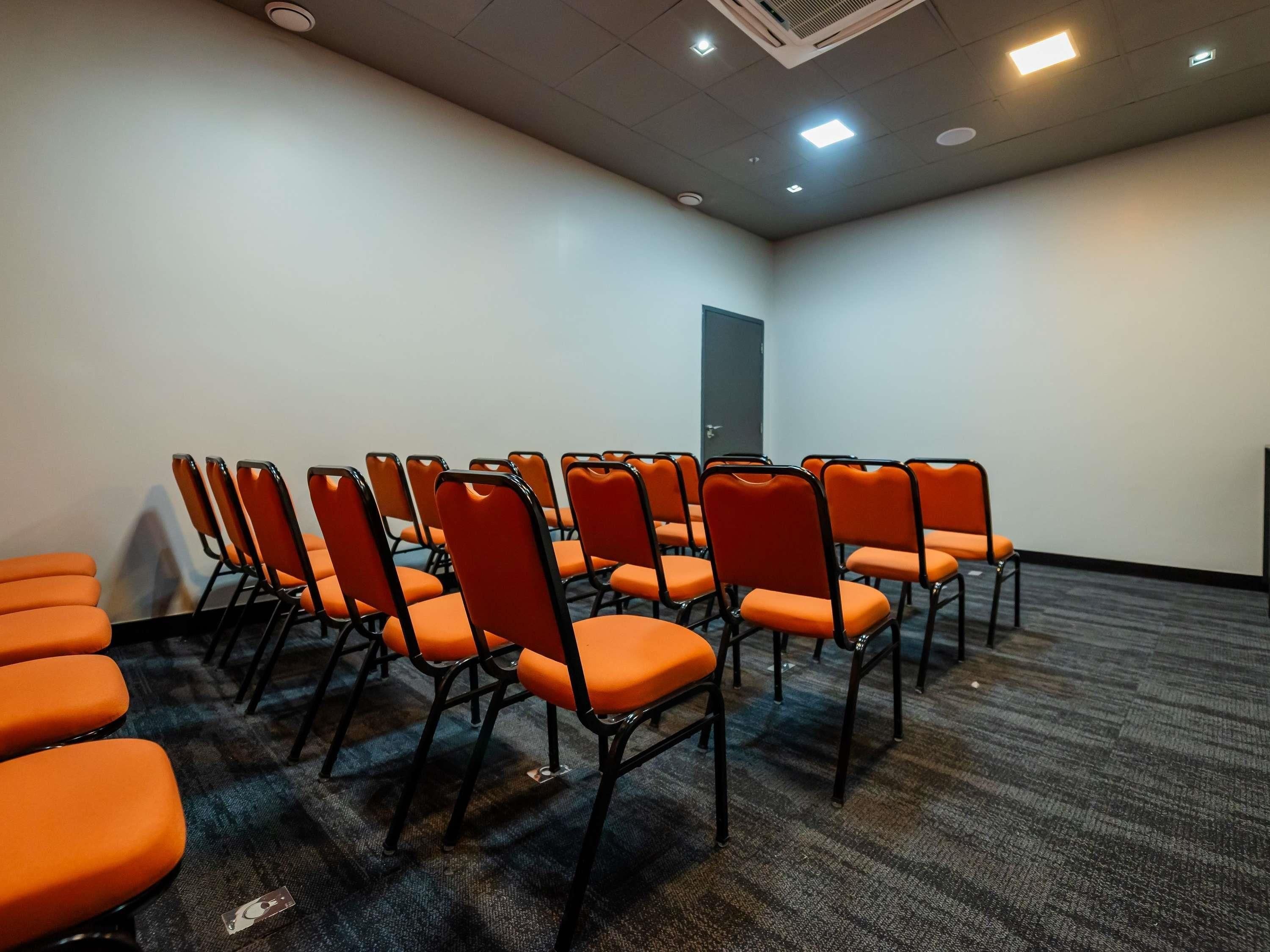 A conference room with rows of orange chairs, a carpeted floor, and a door in the background.