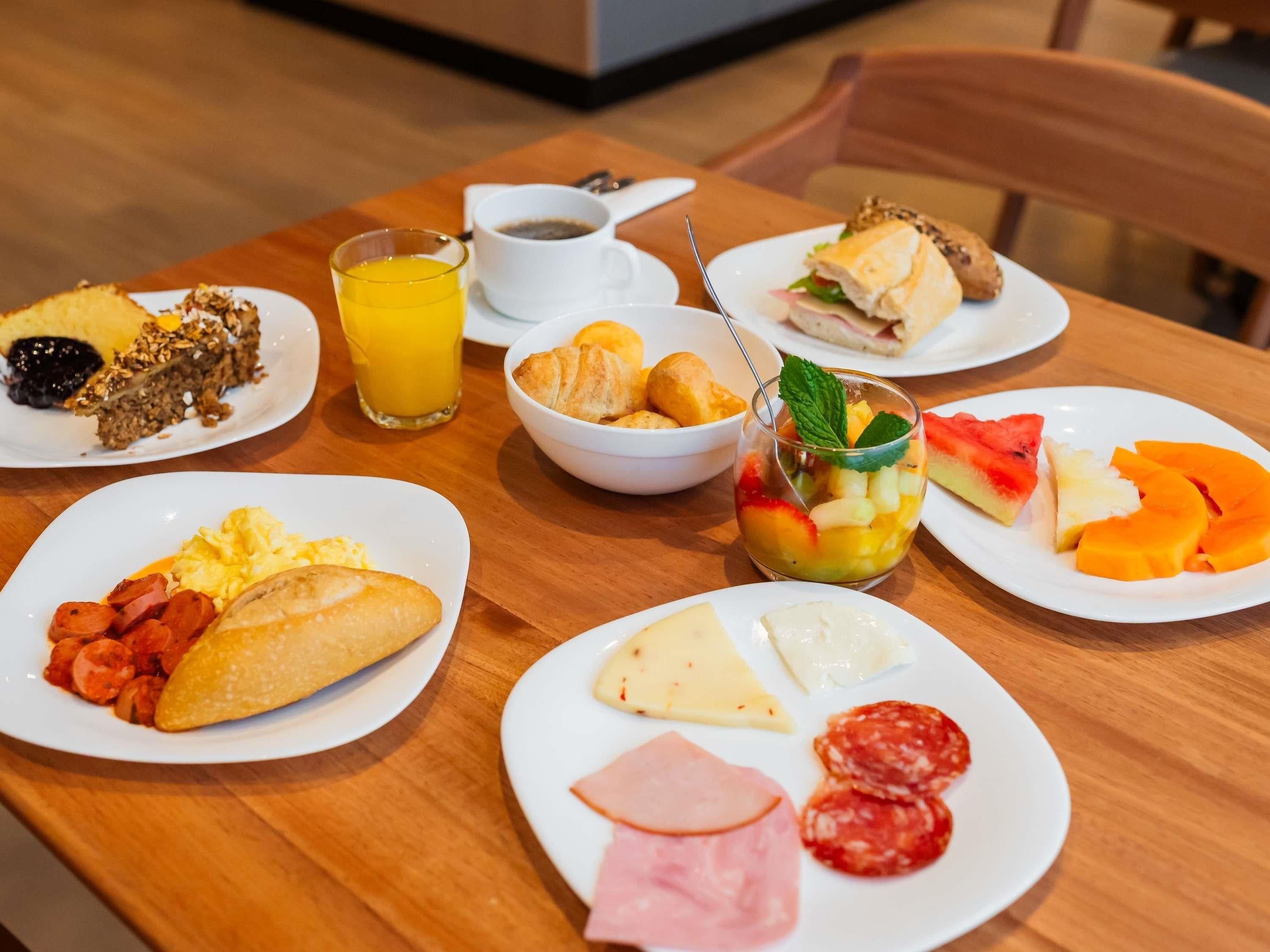 Mesa de café da manhã com pratos de comida, um copo de suco de laranja e uma xícara de café.