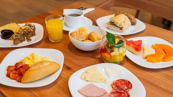 Mesa de café da manhã com pratos de comida, um copo de suco de laranja e uma xícara de café.