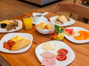 Une table mise pour le petit-déjeuner, avec des assiettes remplies de nourriture, un verre de jus d’orange et une tasse de café.