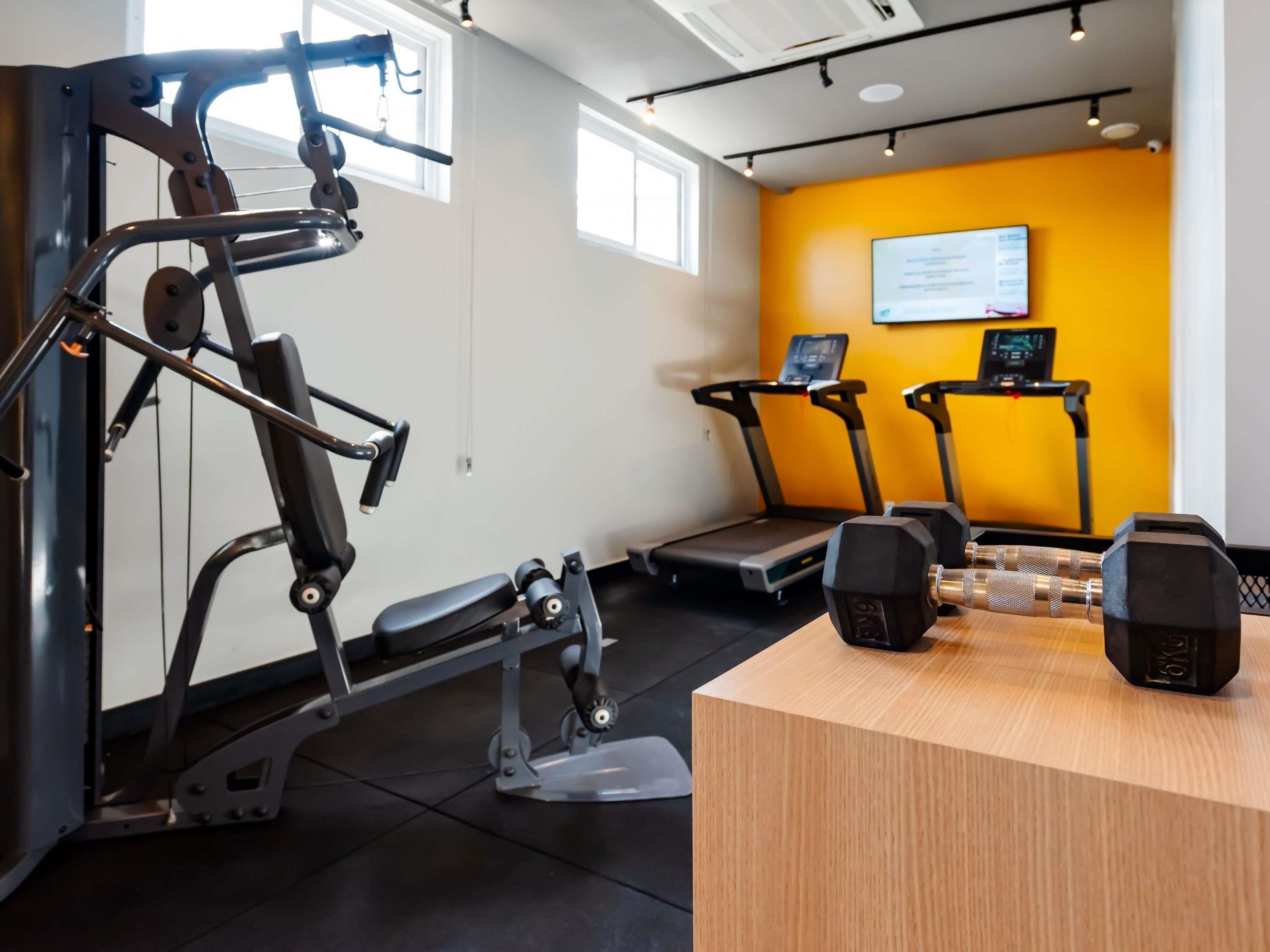 Une salle de sport équipée de matériel d’exercice, de tapis de course et d’un bureau en bois avec des haltères.