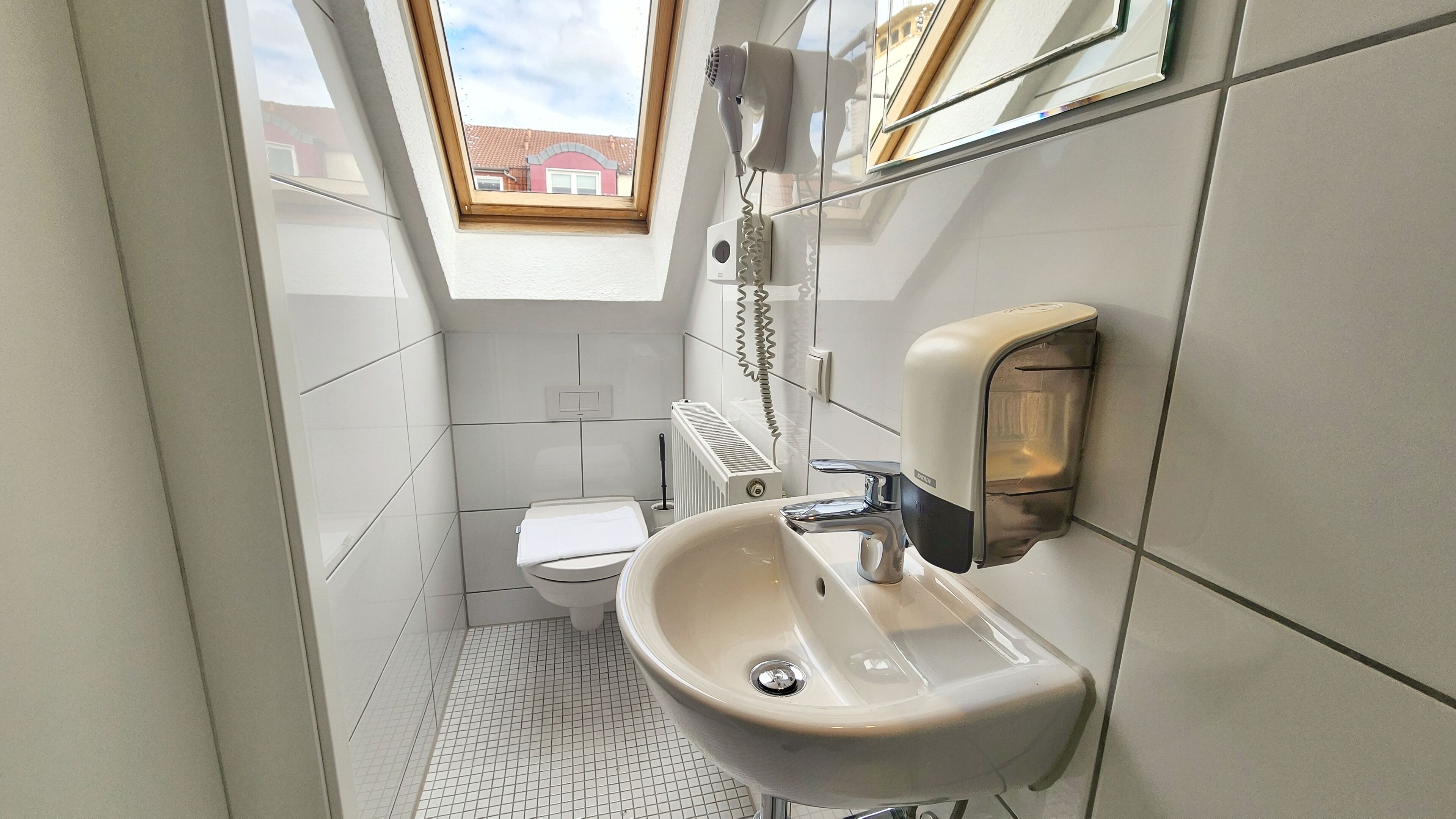 Et lille badeværelse med toilet, håndvask og en hårtørrer fastgjort på væggen.