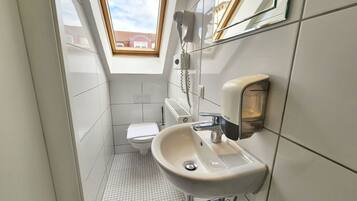 A compact bathroom with a toilet, sink, and a hairdryer mounted on the wall.
