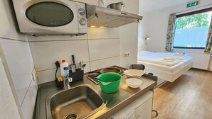 A kitchenette with a sink, a microwave, a stove, and a window with a view of trees. - Aparthotel Marion Weber (Bremen)