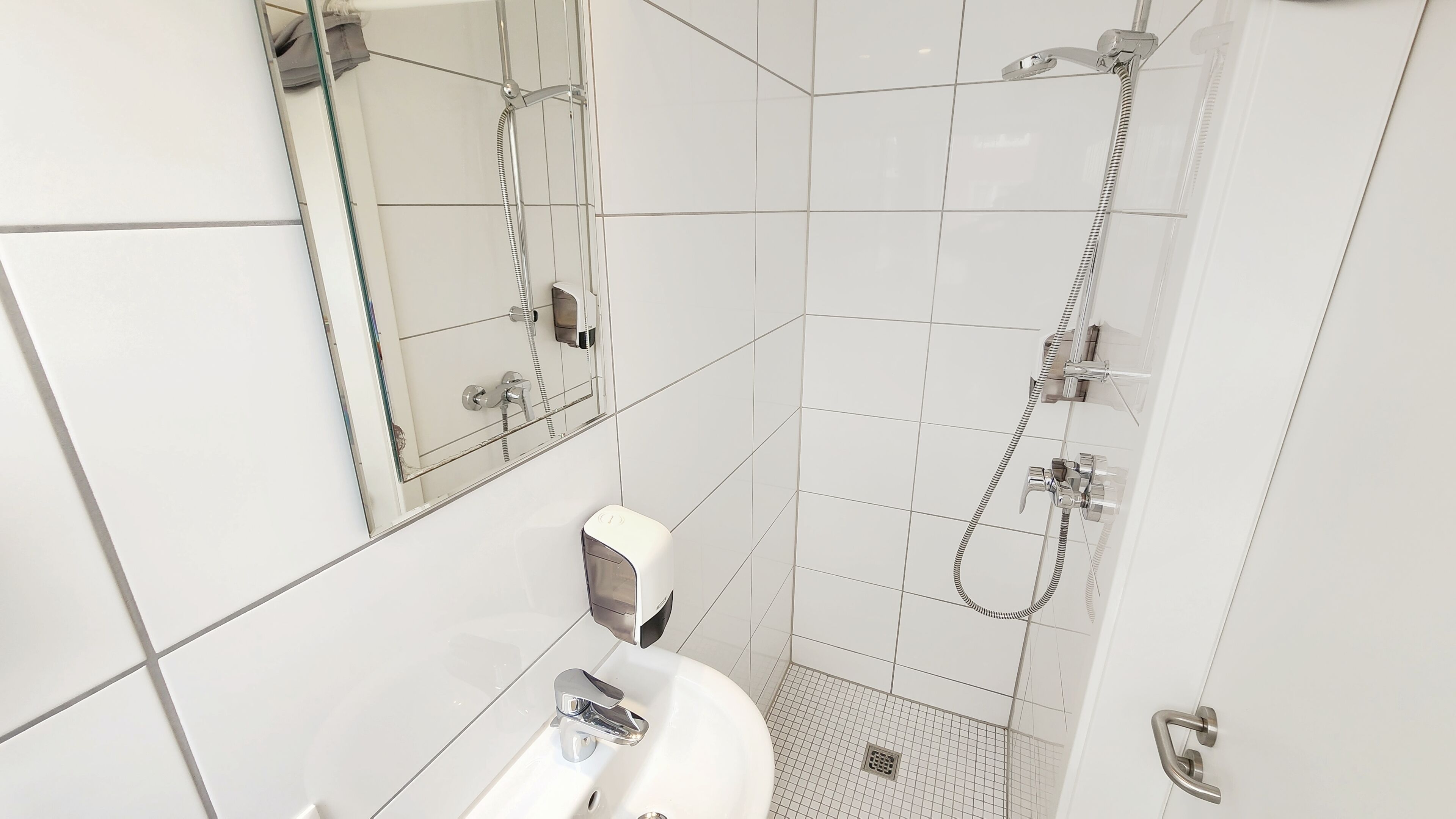 A bathroom with a white sink, a mirror, a shower with a handheld showerhead, and tiled walls.