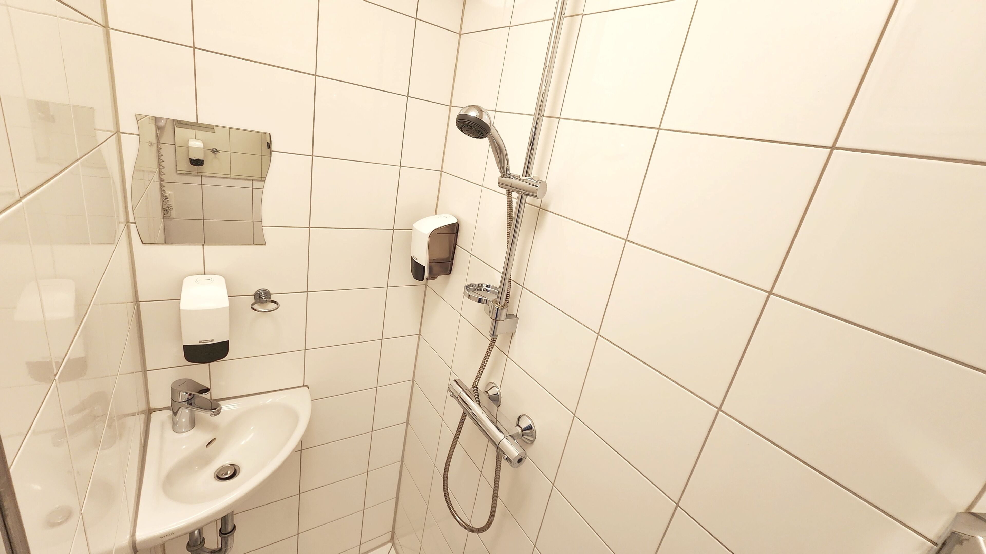 Een badkamer met een wastafel, zeepdispenser en een douche met een handdouche.