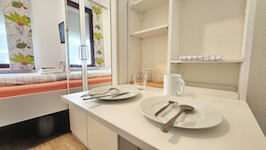 A clean, modern room with a white countertop, a bed with orange bedding, and a window with floral curtains. - Aparthotel Marion Weber (Bremen)