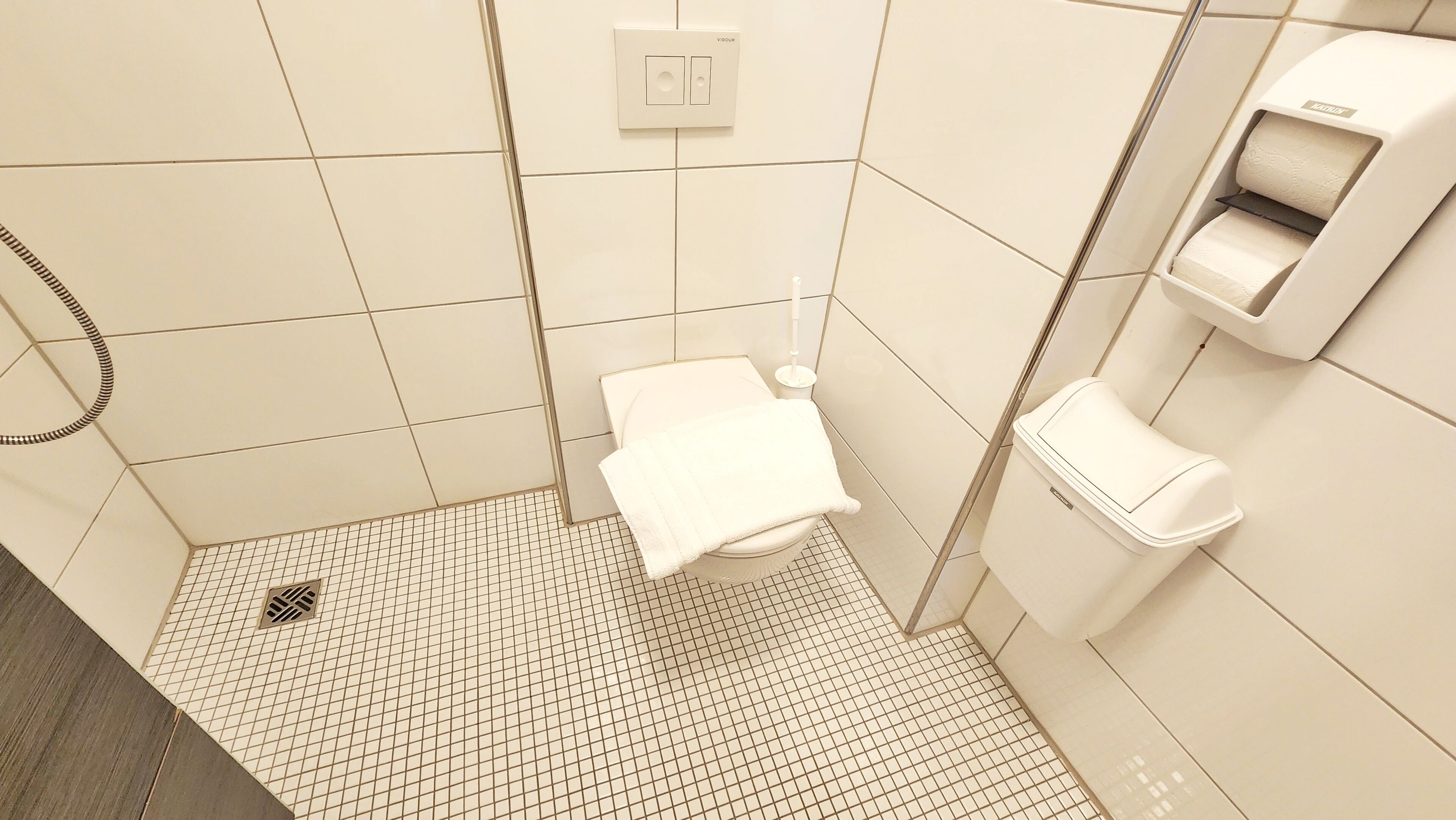 A modern bathroom with a toilet, a hand dryer, and a toilet paper dispenser.