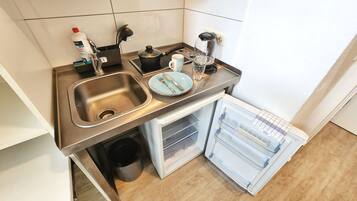 A compact kitchen with a stainless steel sink, a coffee maker, a kettle, and a refrigerator.