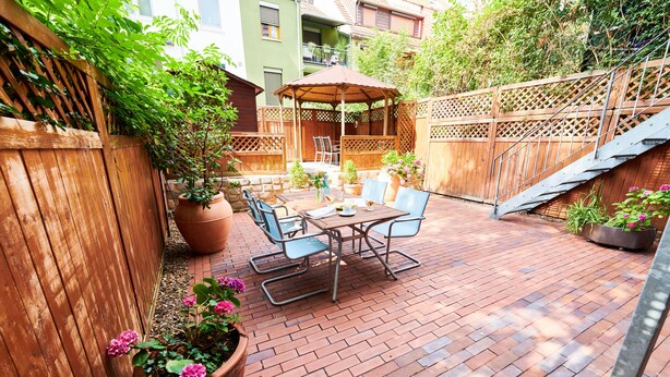 A patio with a wooden fence, a covered seating area, and potted plants. - Aparthotel Marion Weber (Bremen)