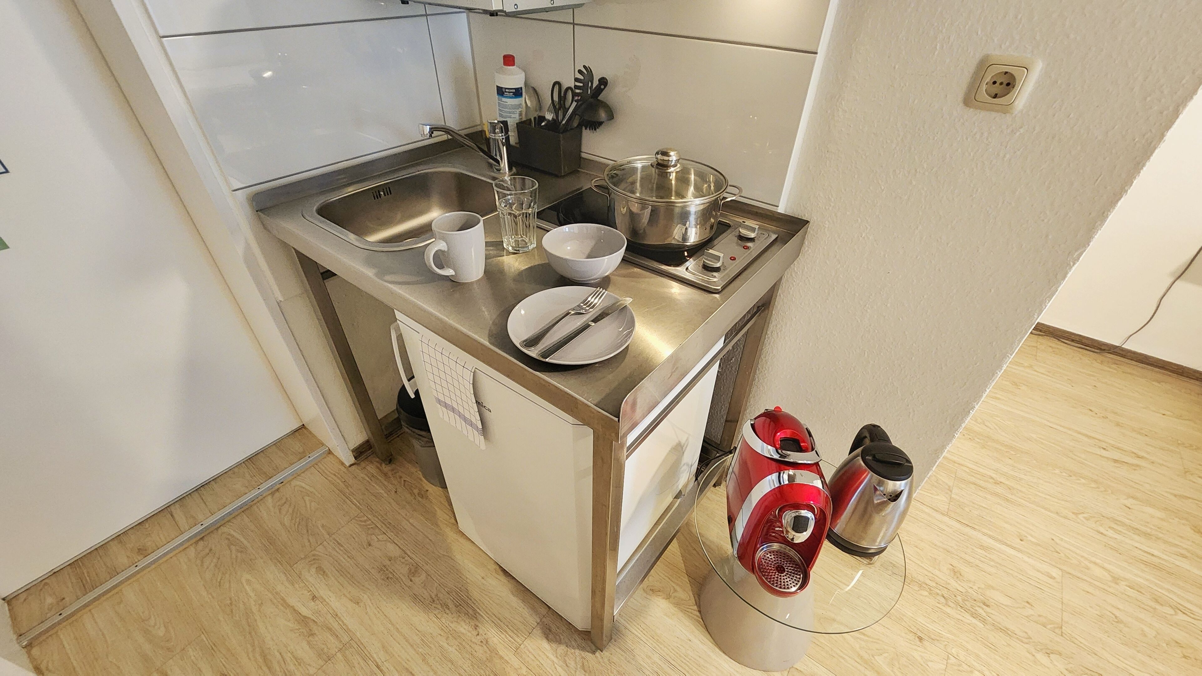 Eine kleine Küche mit Spüle, Herd, Wasserkocher und einer Arbeitsplatte, auf der eine Tasse, eine Schüssel und ein Teller stehen.
