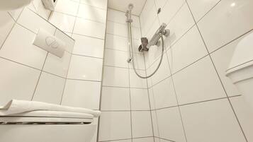 A bathroom with white tiles, a shower, a towel rack, and a toilet.