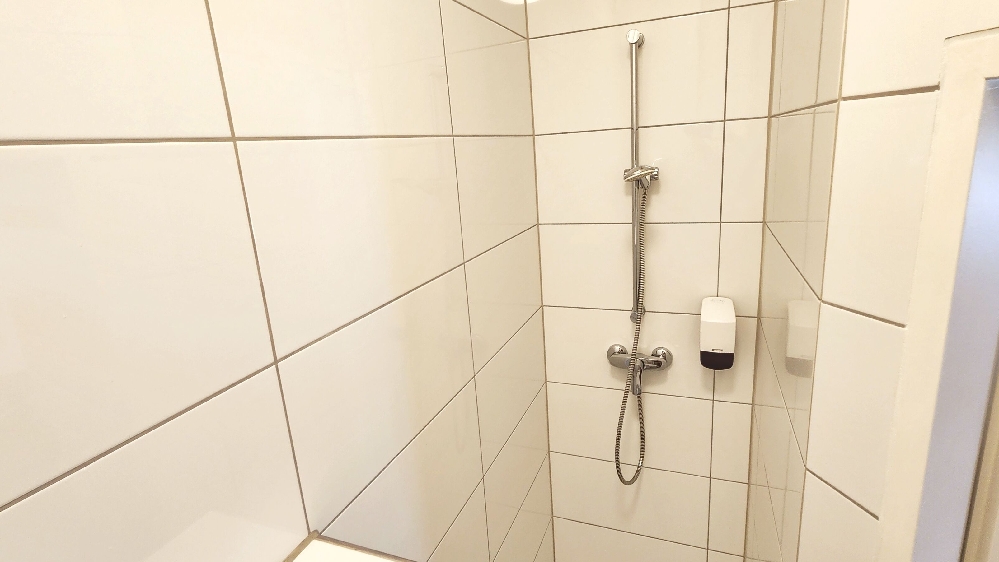 A shower with a handheld showerhead and a wall-mounted faucet.
