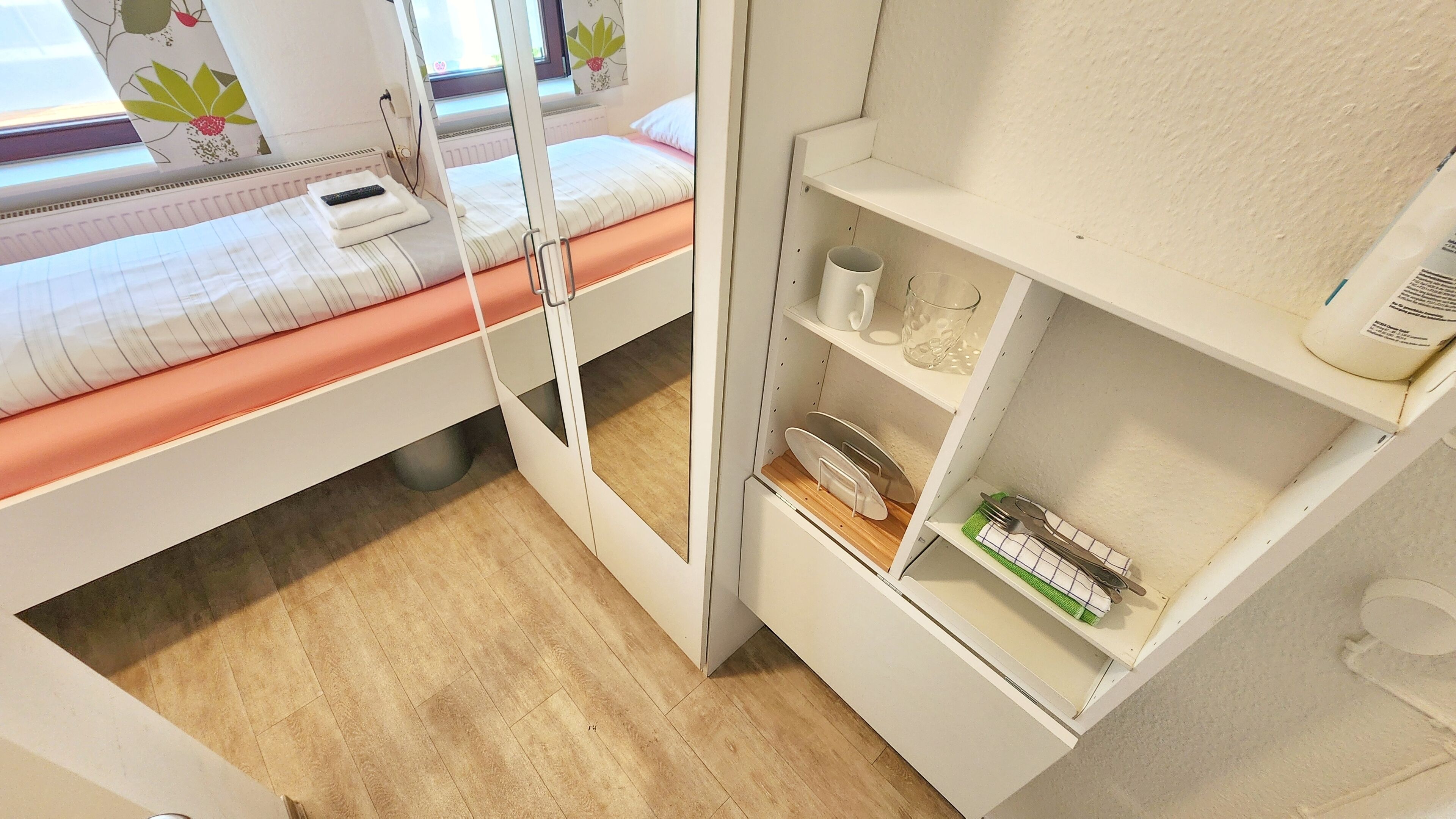 Een kleine kamer met een bed, een klein plankje met toiletartikelen en een raam met uitzicht.