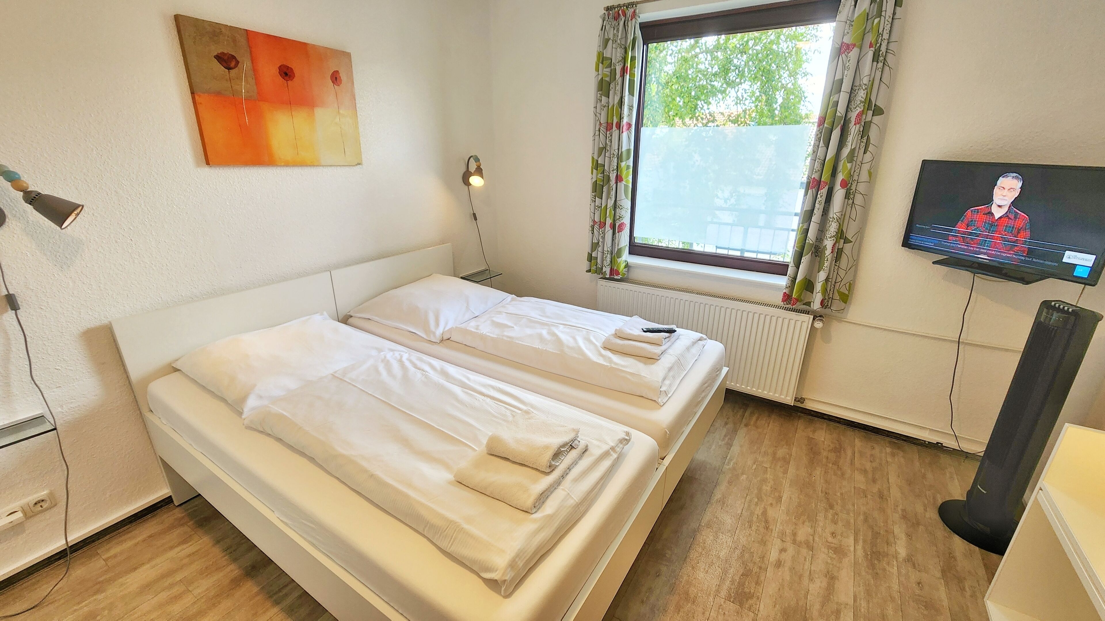 Une chambre d’hôtel avec deux lits, une télévision, un radiateur et une fenêtre avec des rideaux.