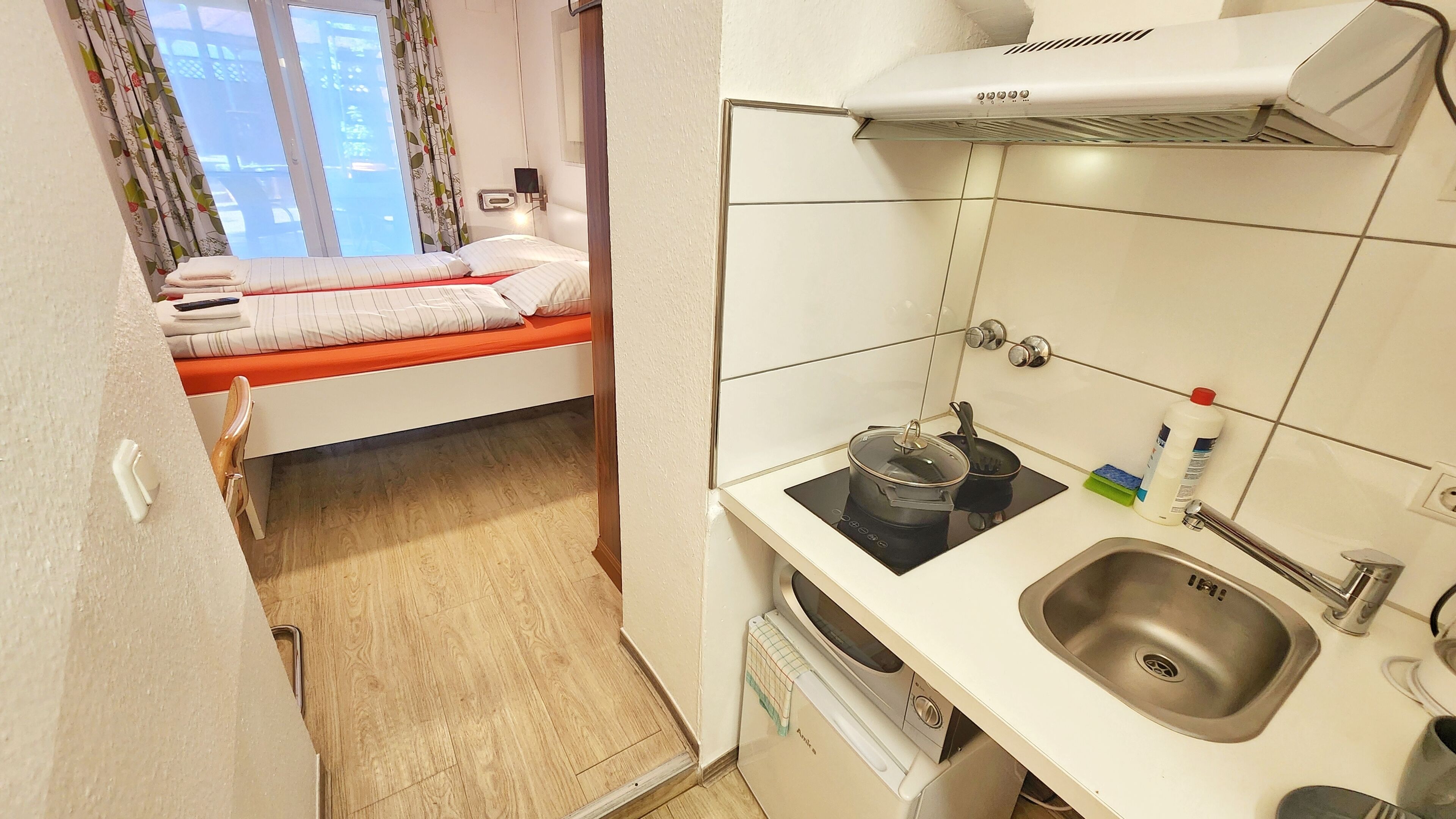 A compact kitchenette with a stove, sink, and a small window with curtains.