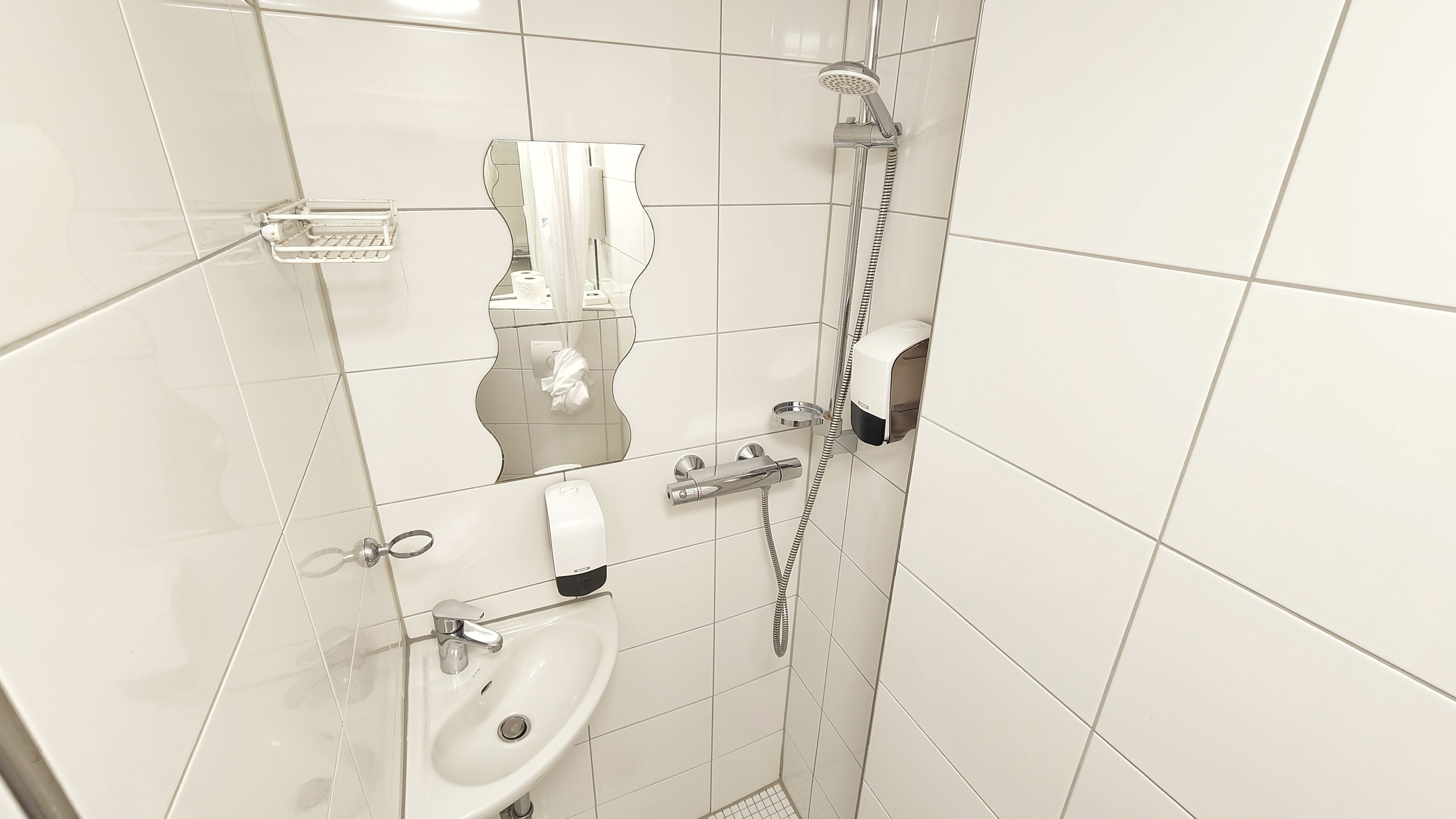 Un baño con azulejos blancos, un lavabo, un inodoro, una ducha y un perchero para toallas.