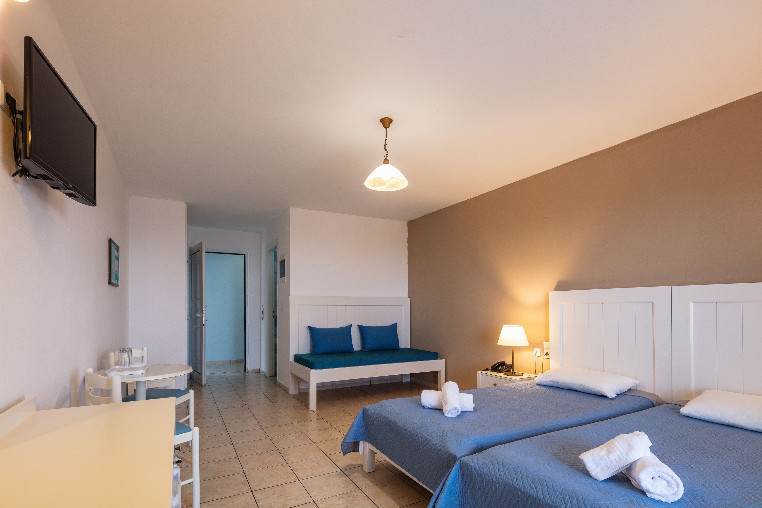 A hotel room with two beds, a desk, a chair, a TV, and a lamp.