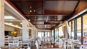 Ein geräumiges Restaurant mit hohen Decken, Holzbalken und großen Fenstern. Die Tische sind ordentlich mit weißen Stühlen angerichtet.