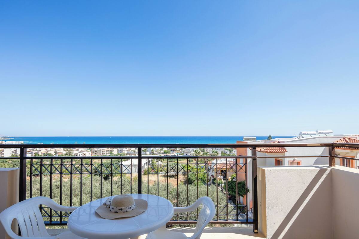 Un balcon avec une table et des chaises, offrant une vue sur la côte, avec des bâtiments et la mer.