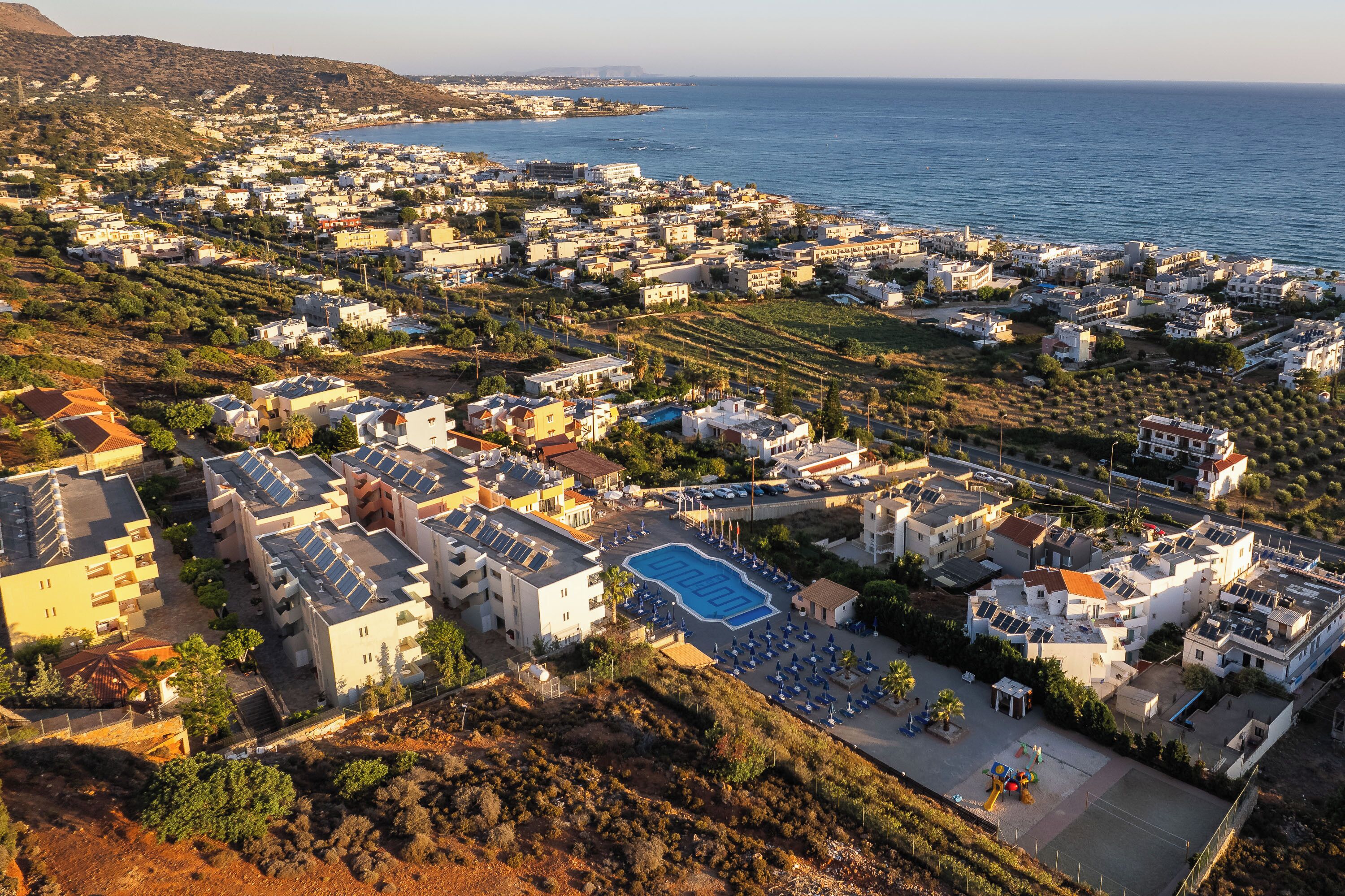 Vista aérea de una zona residencial costera con casas, una piscina y paneles solares.