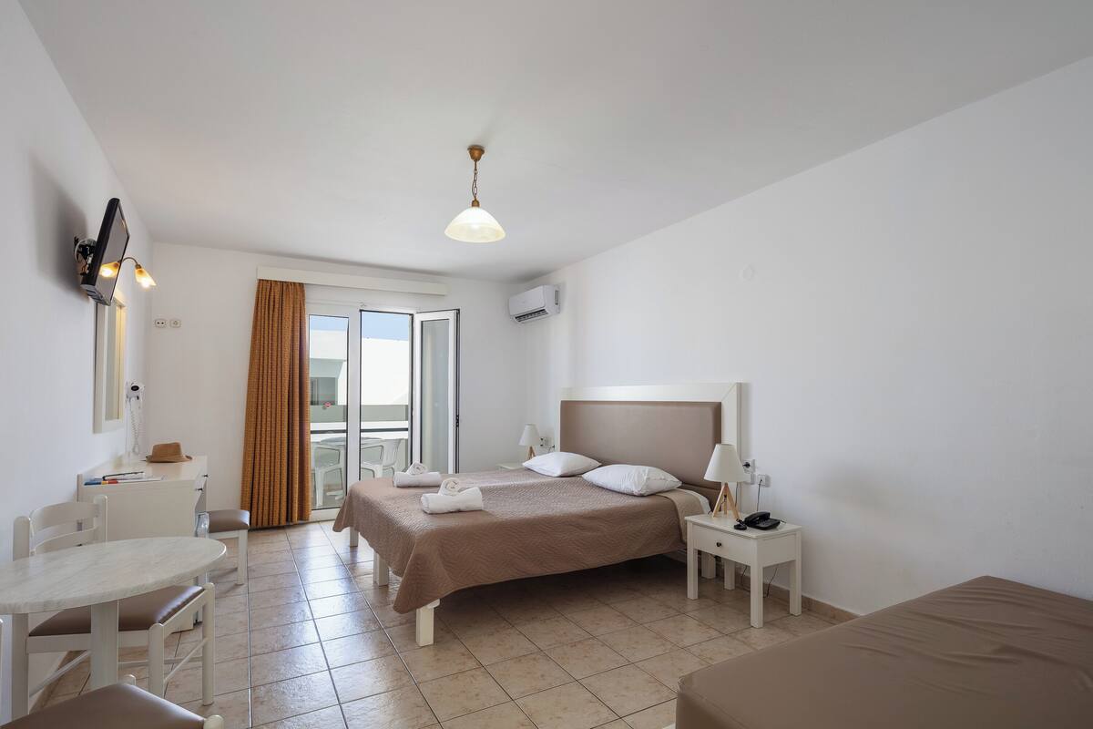 Une chambre d’hôtel comprenant un lit, un bureau, une chaise, une table, une lampe, un téléphone et une fenêtre avec des rideaux.