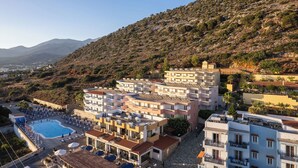 Ein Hotel an der Küste mit mehreren Etagen, einem Schwimmbad und Blick auf das Meer und die Hügel.