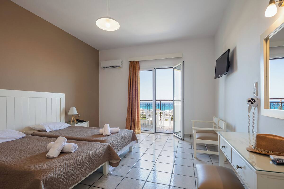 Une chambre d’hôtel avec deux lits, un bureau, une chaise, une télévision et un balcon donnant sur la mer.