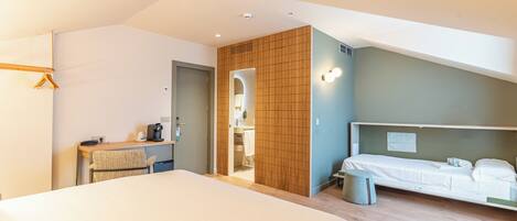 Una habitación de hotel moderna con una cama grande, un escritorio con una silla, un taburete pequeño y un baño visible a través de una puerta abierta.
