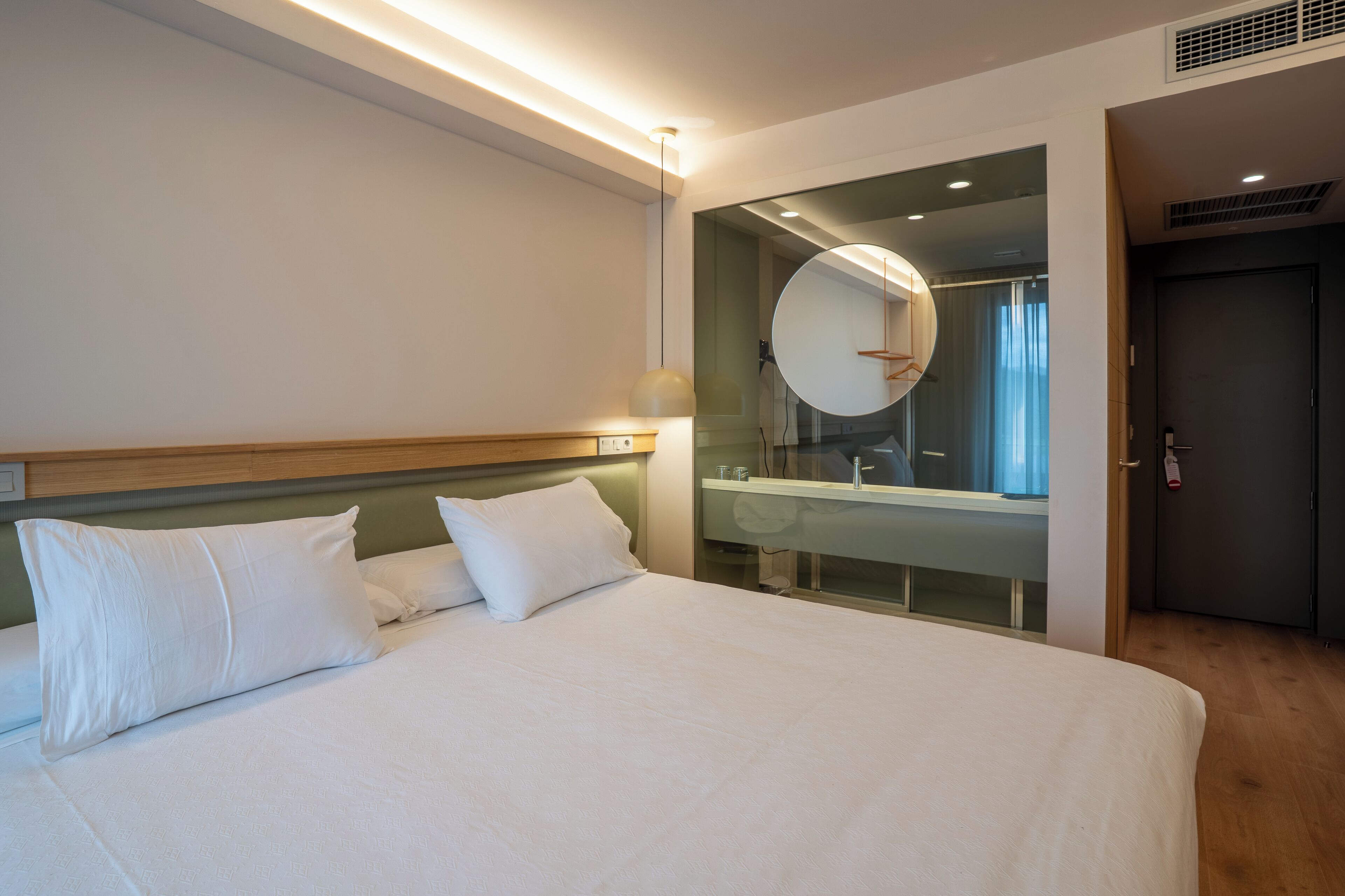 A modern hotel room with a large bed, a bedside table, a mirror, and a view of the bathroom.