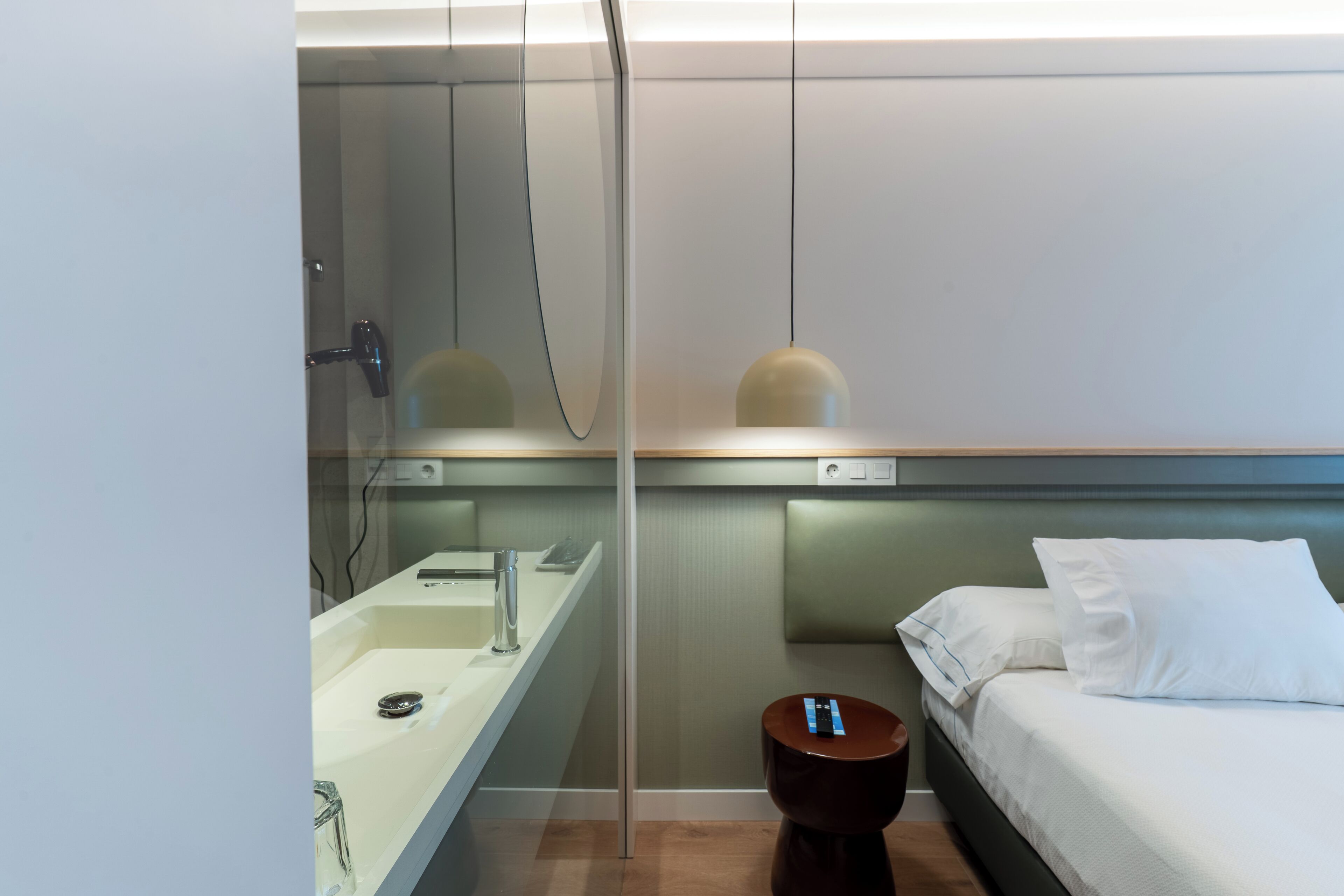 A modern bathroom with a glass shower enclosure, a sink, and a bedside table with a mirror.