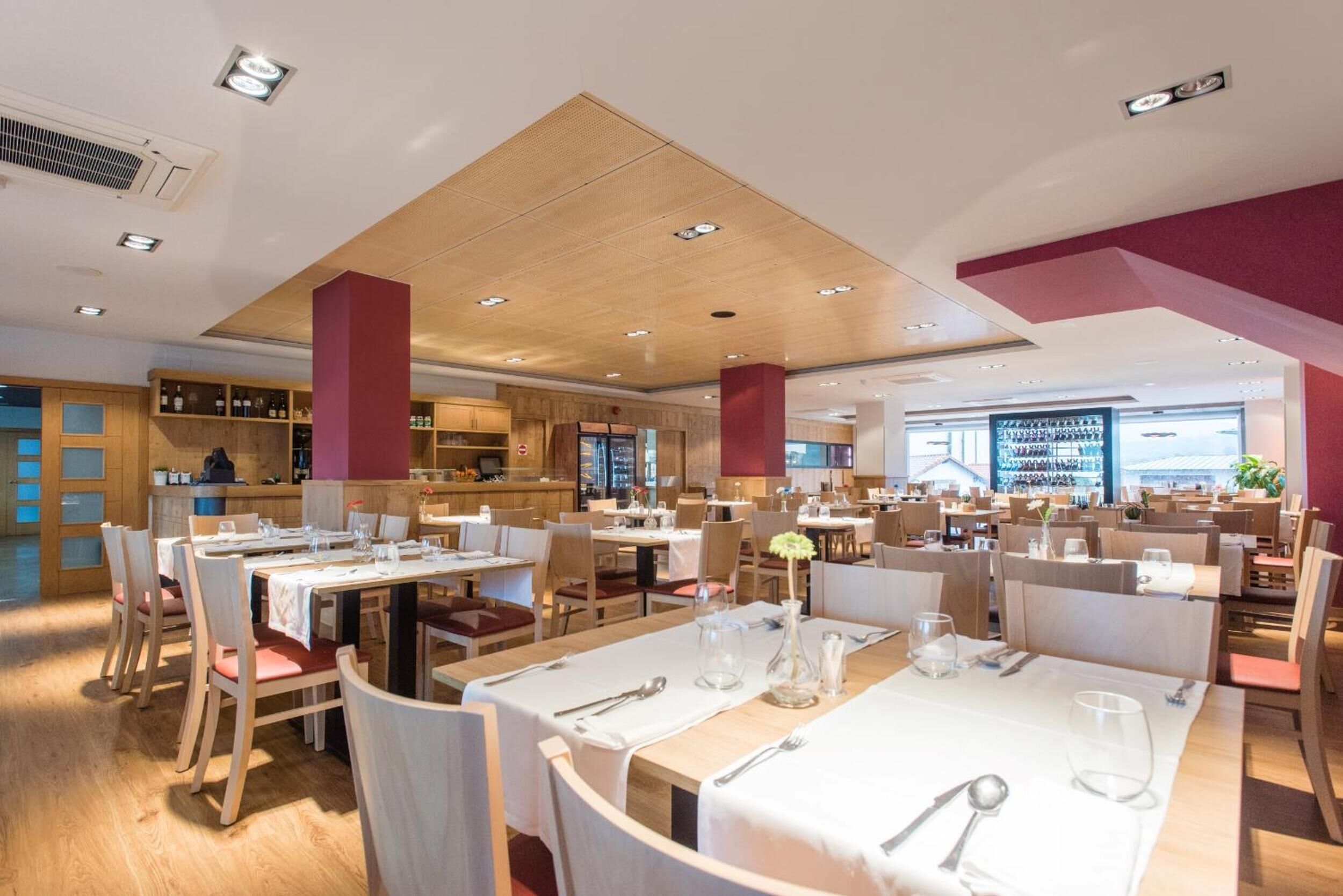 A spacious restaurant with multiple dining tables and chairs, a bar area, and a view of the cityscape.