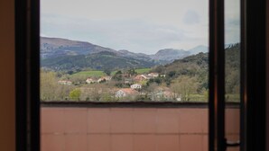 Une vue depuis un balcon dont le sol est recouvert de carreaux bruns, donnant sur un paysage composé de maisons et de collines.