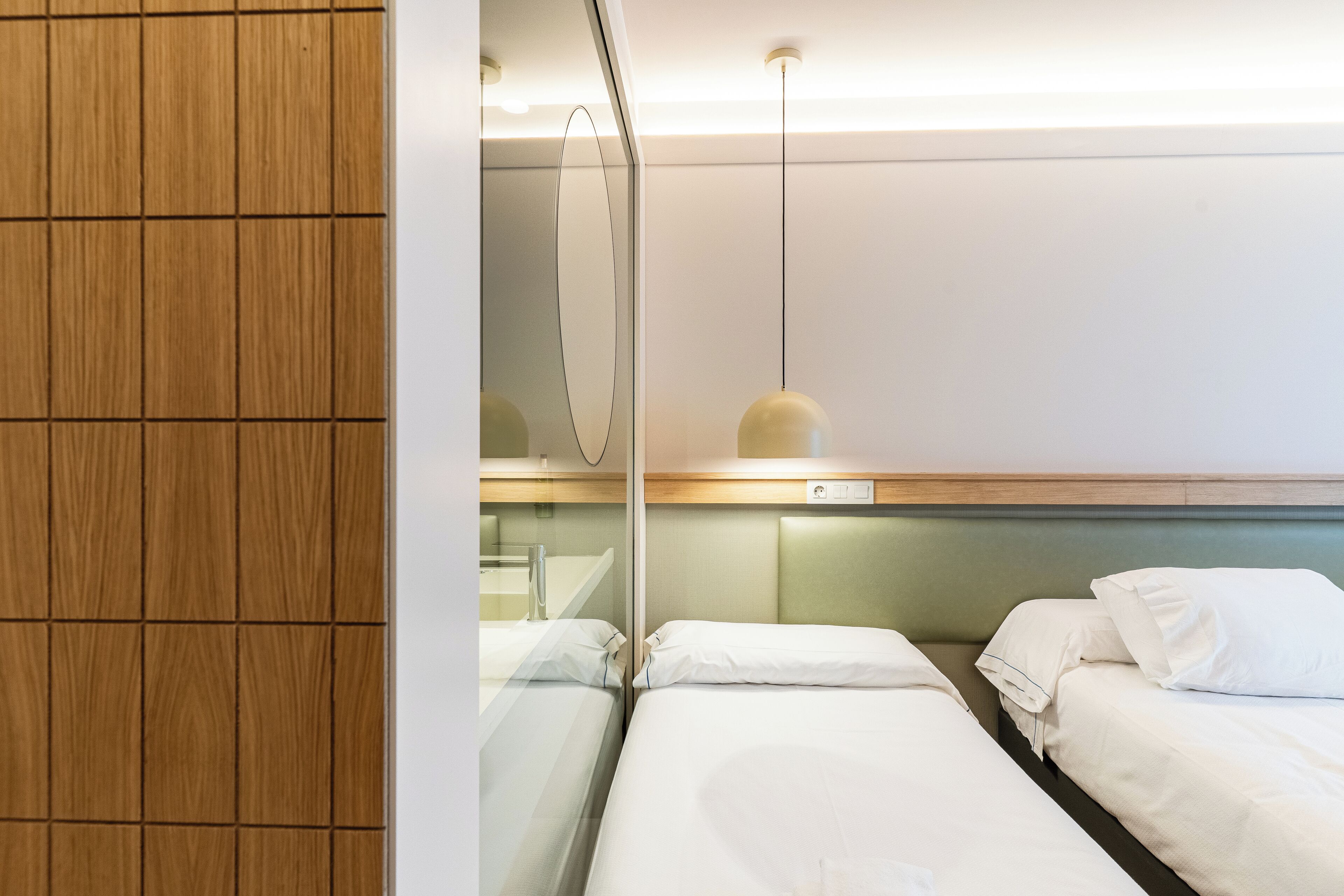 Habitación de hotel con dos camas, un panel de madera, un espejo y una lámpara colgante.