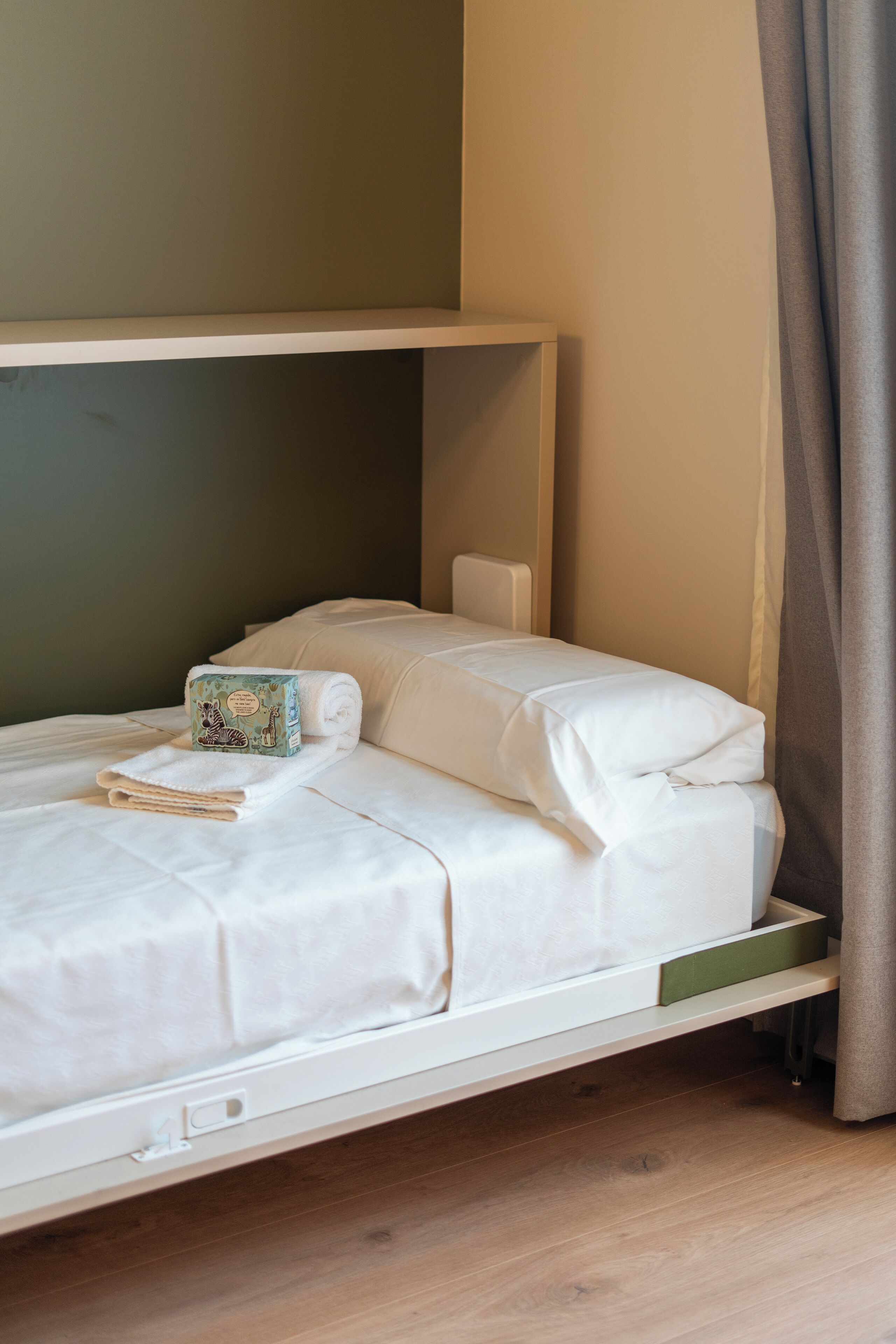 Een net opgemaakt bed met een opgerolde handdoek en een set toiletartikelen.