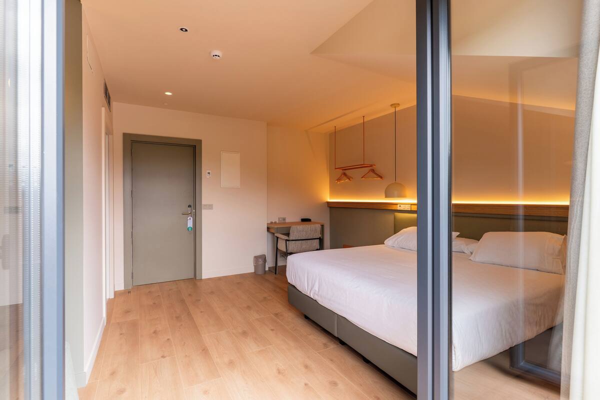 A modern hotel room with a large bed, a desk, and a small seating area.