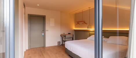 A modern hotel room with a large bed, a desk, and a small seating area.