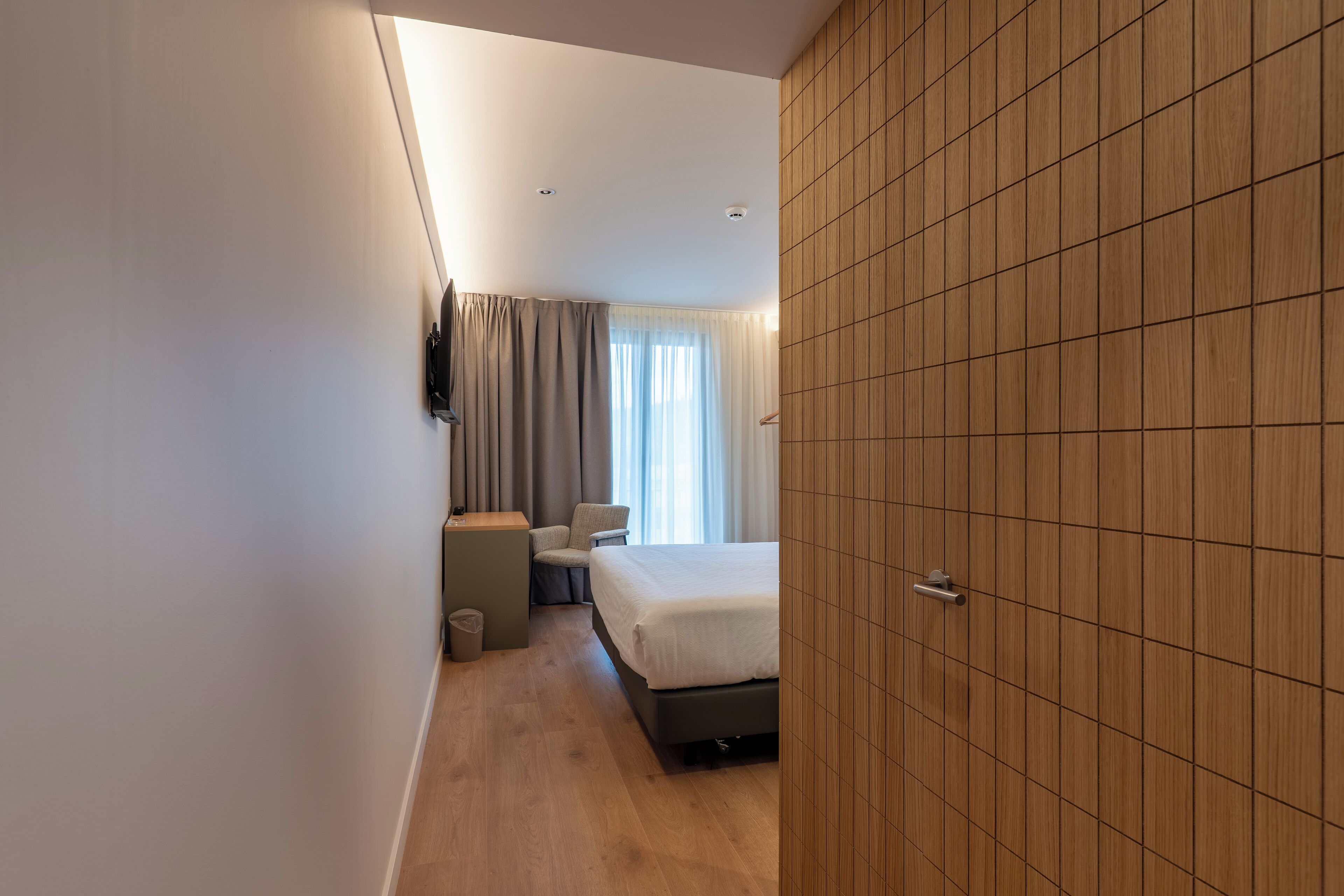 Una habitación de hotel moderna con una cama, un escritorio, una silla y un televisor instalado en la pared.