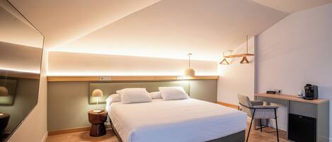 A modern hotel room with a large bed, bedside table, desk, and chair.