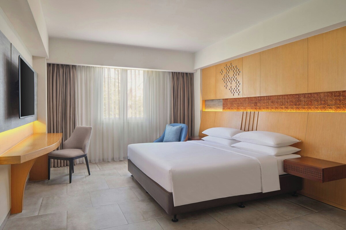 A hotel room with a bed, a desk, a chair, a TV, and a window with curtains.