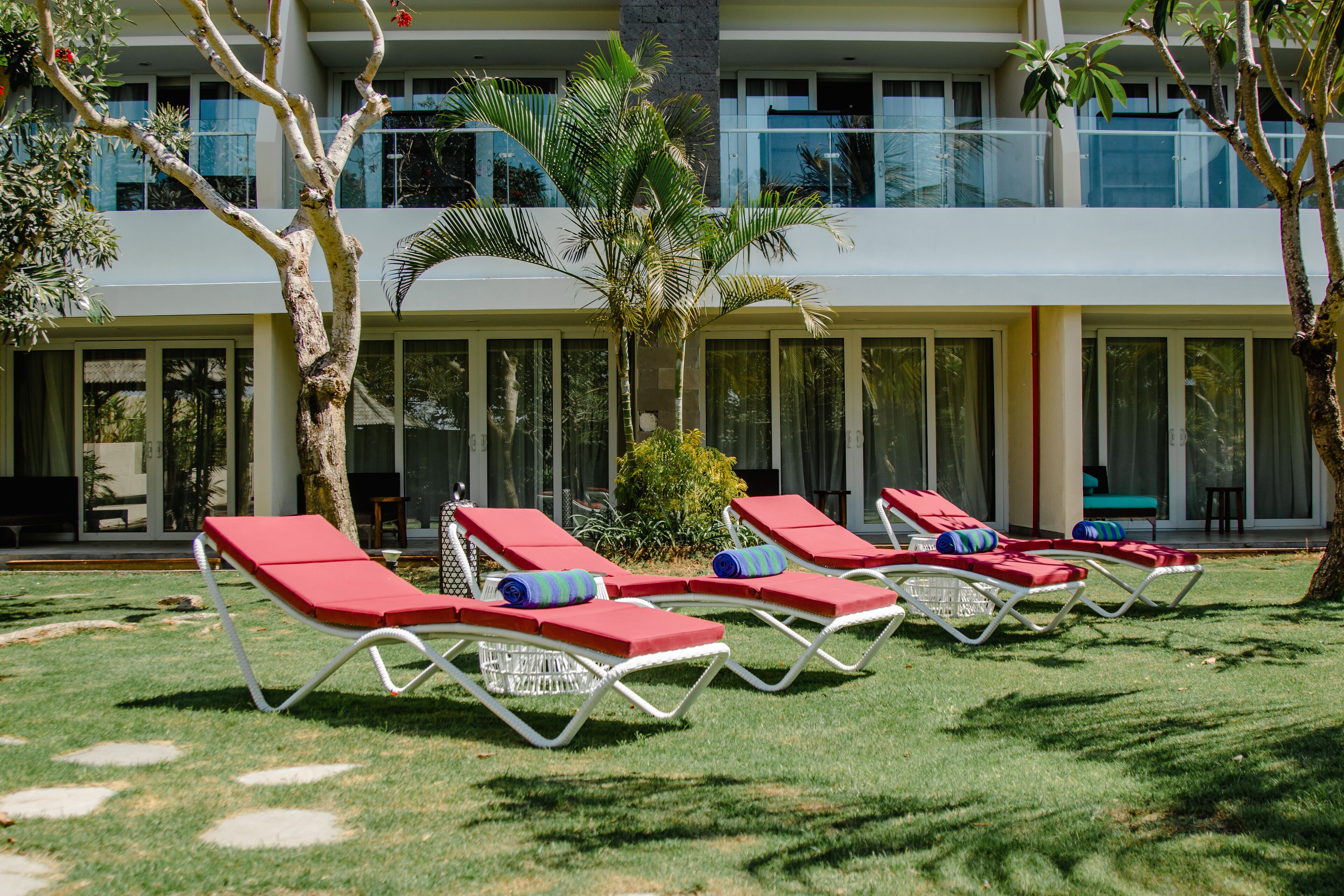 A poolside area with red lounge chairs, a palm tree, and a modern building with large windows.