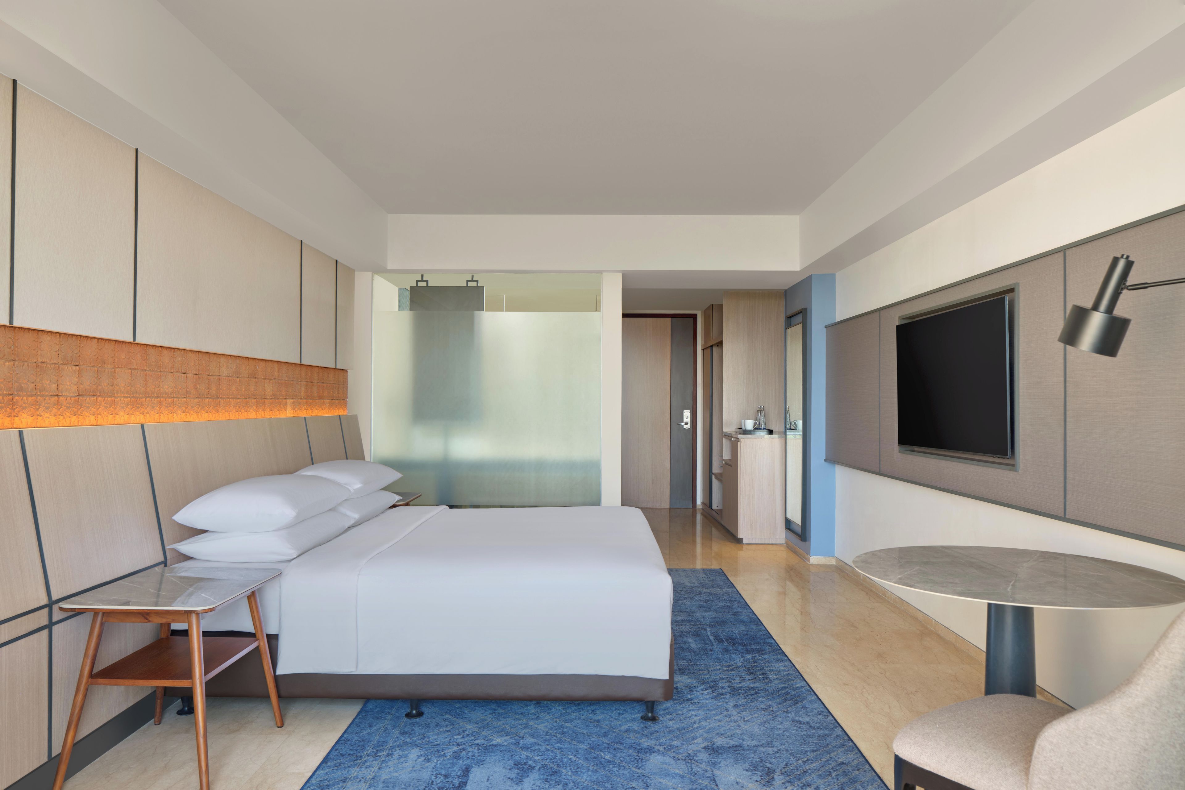 Une chambre d’hôtel moderne avec un grand lit, des tables de chevet, un bureau, une chaise, une télévision et une salle de bain visible à travers une porte.
