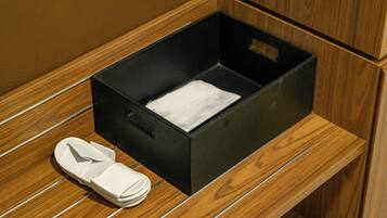 A black storage box on a wooden surface with a pair of white slippers beside it.