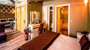 Habitación de hotel con cama, escritorio con espejo, armario y zona de ducha.