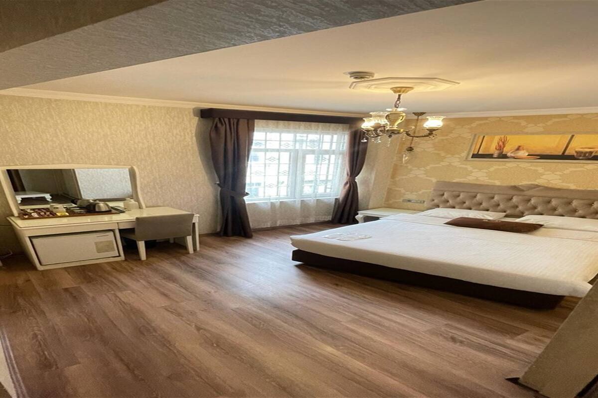 Habitación de hotel con una cama grande, un escritorio con espejo, una araña y una ventana con cortinas.