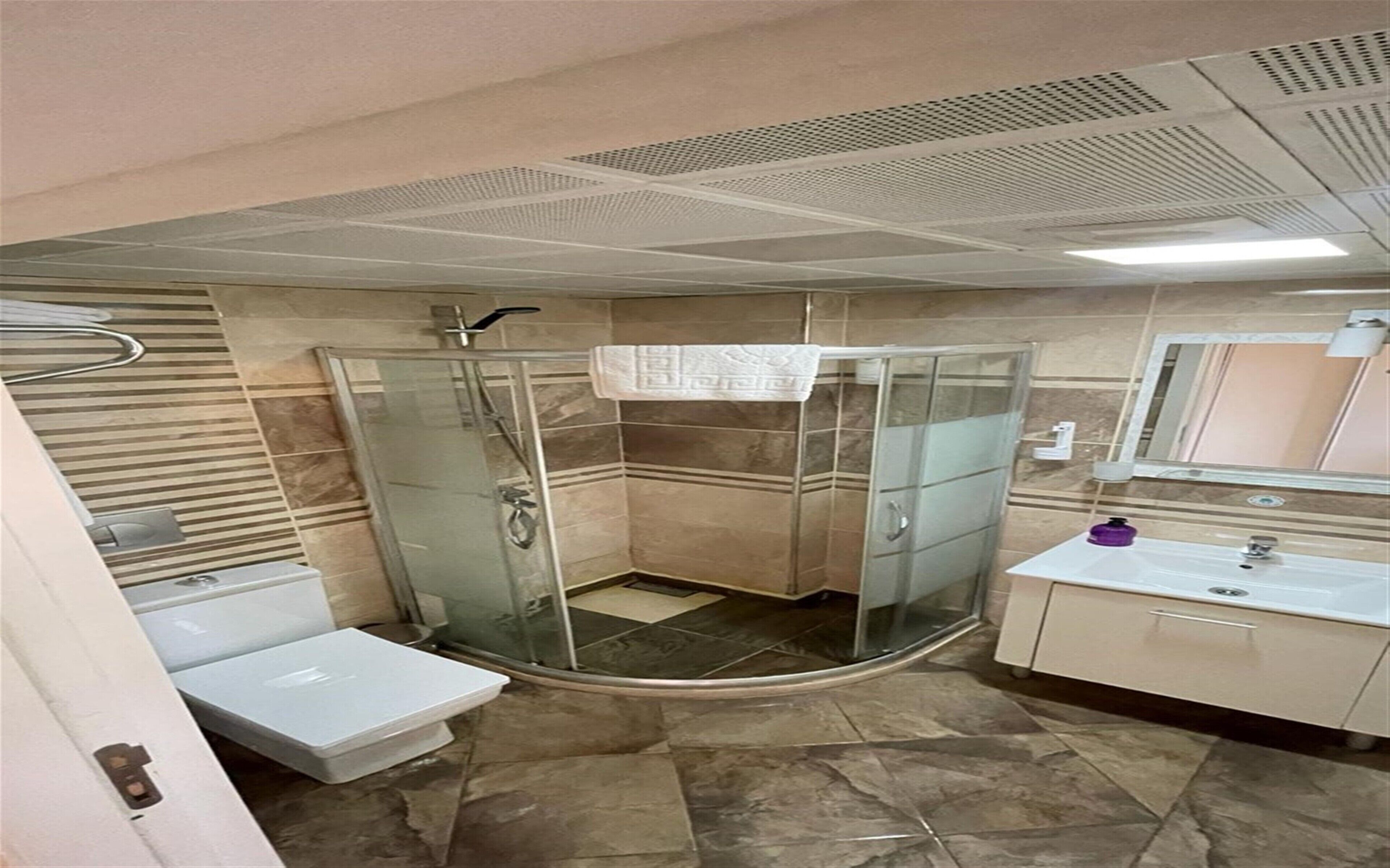 Een badkamer met een douchecabine van glas, een witte wastafel en een spiegel.